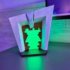 May include: A decorative, geometric light fixture with a green glowing center. The fixture has a white frame with vertical lines and a brown, brick-like interior. The base is black, and the overall design is modern and artistic.