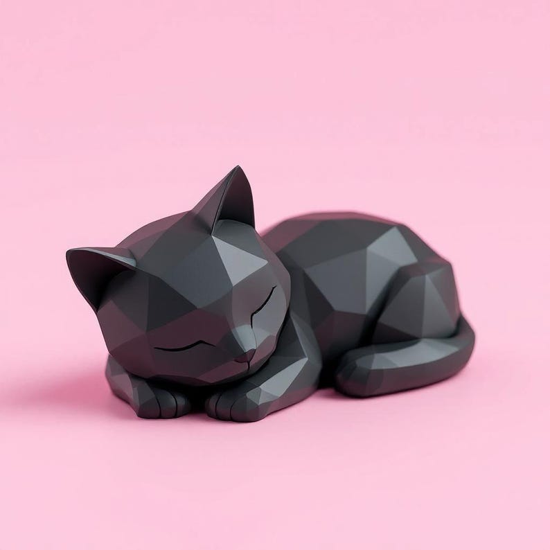 May include: A geometric, sleeping cat sculpture in dark gray, resting on a pink surface. The cat's form is composed of angular facets, giving it a modern, stylized appearance. The cat's eyes are closed, suggesting peaceful slumber.