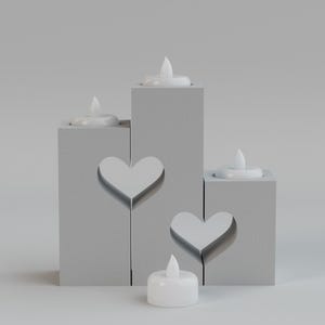 May include: A set of four gray candle holders with heart cutouts and white LED candles. The candle holders are arranged at different heights, creating a tiered effect. The candles are lit, casting a soft glow.