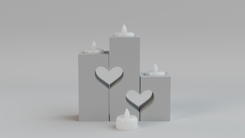 May include: A set of four gray candle holders with heart cutouts and white LED candles. The candle holders are arranged at different heights, creating a tiered effect. The candles are lit, casting a soft glow.
