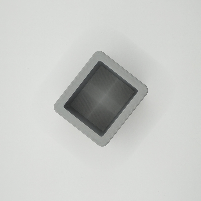 Pu&ograve; includere: Un contenitore quadrato grigio con interno incassato. Il contenitore ha una finitura liscia e opaca ed &egrave; posto su uno sfondo bianco. Il design &egrave; semplice e moderno, con linee pulite e un'estetica minimalista.