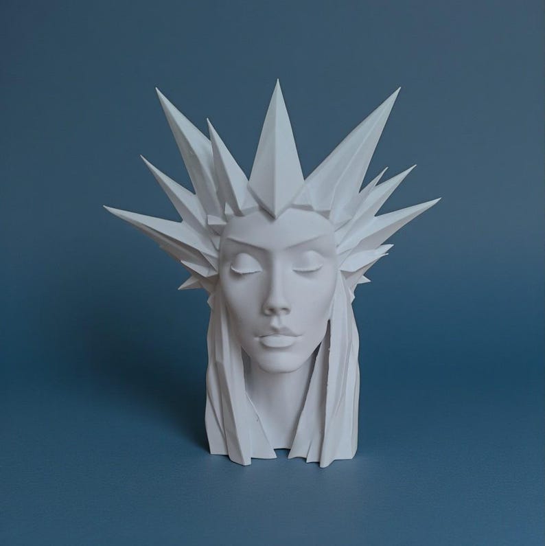 May include: A white sculpture of a woman's face with closed eyes and a crown of sharp, geometric shapes. The sculpture has long hair and is set against a blue background. The artwork is a bust, showcasing the head and upper shoulders.
