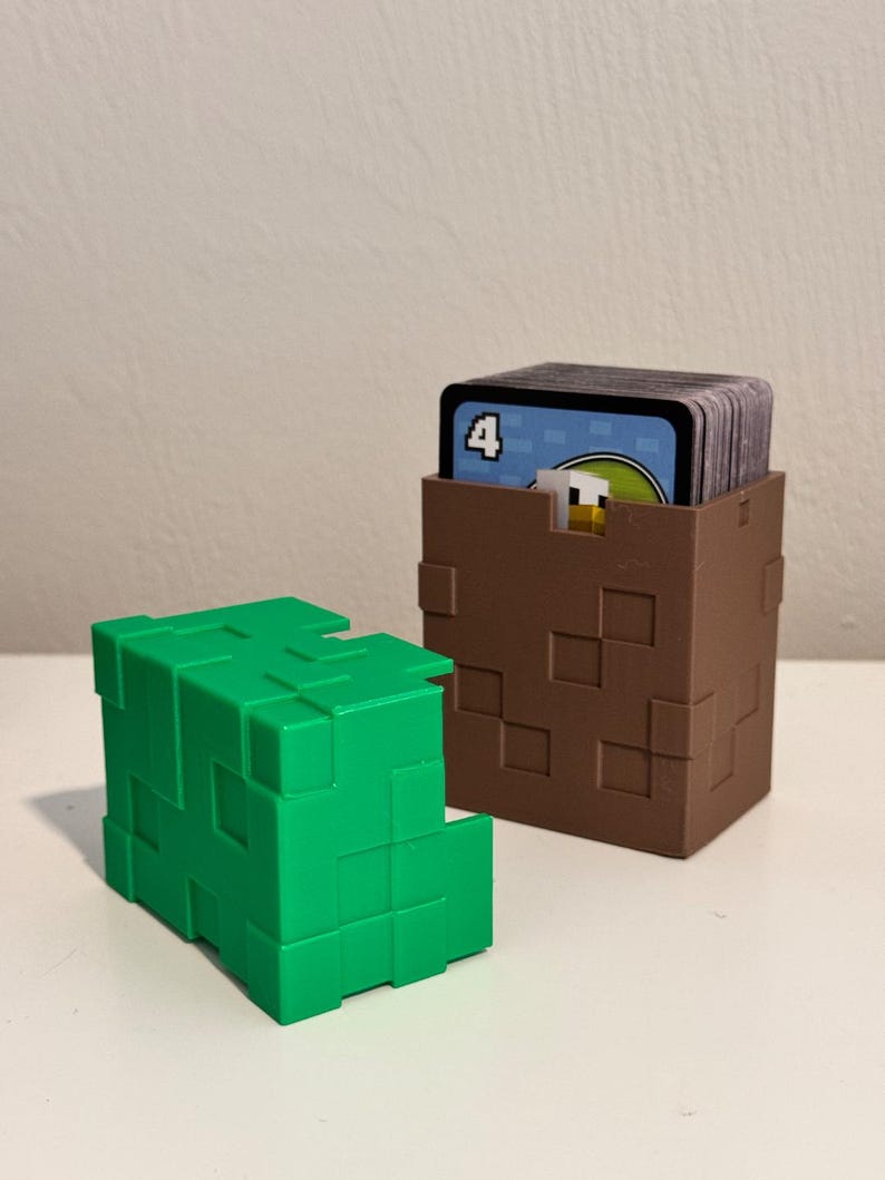 May include: Two cube-shaped card holders. One is bright green, the other is brown and contains a stack of cards. The holders have a pixelated design, with square cutouts. The cards have a blue background and a number 4.