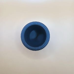 May include: A small, round, blue container with a textured, ridged exterior. The interior is a darker shade of blue. The container is likely made of ceramic or a similar material. The object is viewed from above.
