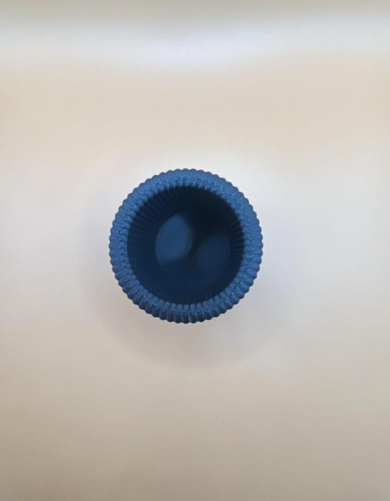 May include: A small, round, blue container with a textured, ridged exterior. The interior is a darker shade of blue. The container is likely made of ceramic or a similar material. The object is viewed from above.
