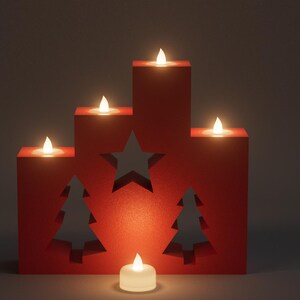 May include: A red, tiered Christmas decoration with cut-out star and tree shapes, illuminated by five battery-operated candles. A single candle sits in front. The warm glow creates a festive ambiance, perfect for holiday decor.