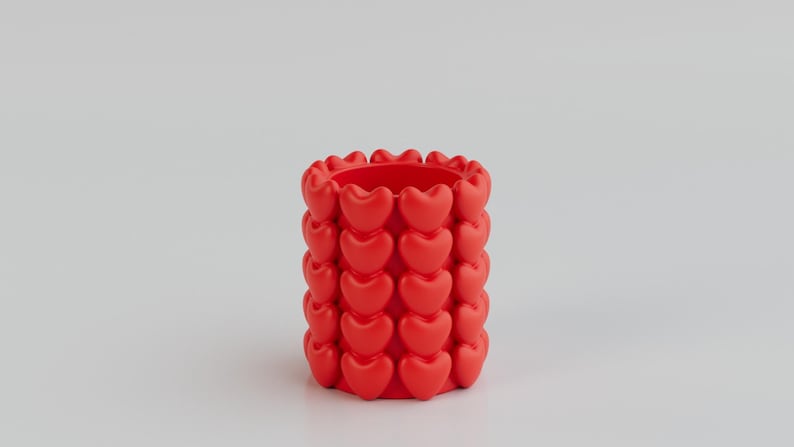 May include: A vibrant red cylindrical container adorned with rows of heart-shaped designs. The container is a solid color and has a smooth texture. The design is repeated around the entire container. This decorative item could be used as a pencil holder or small vase.