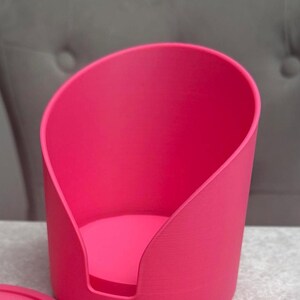 May include: A vibrant pink pet bed with a distinctive curved design. The bed is made from a solid material and features a rounded base. The minimalist design is suitable for small pets, with a modern aesthetic.