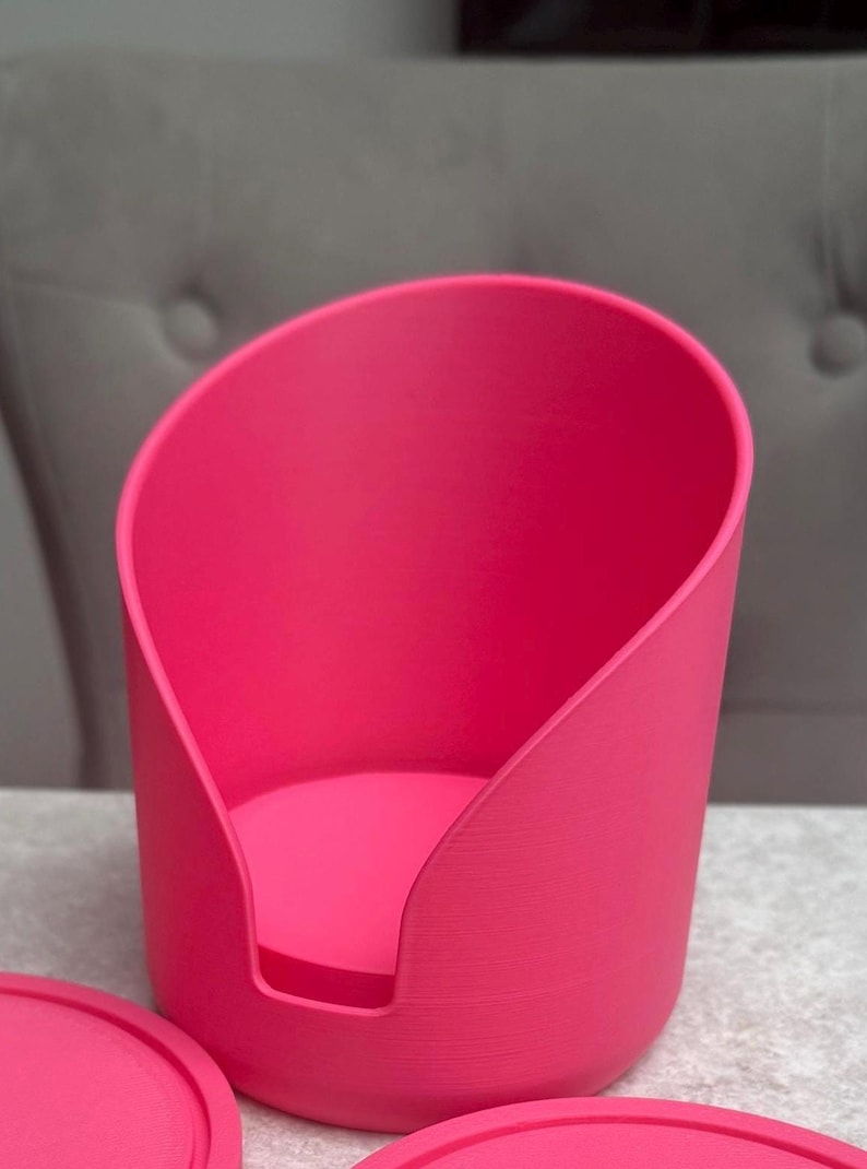May include: A vibrant pink pet bed with a distinctive curved design. The bed is made from a solid material and features a rounded base. The minimalist design is suitable for small pets, with a modern aesthetic.