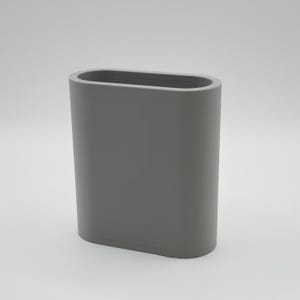 May include: A gray, oval-shaped container with a smooth surface. The container has rounded edges and a rectangular opening at the top. The object is a solid, neutral color and appears to be made of a durable material.