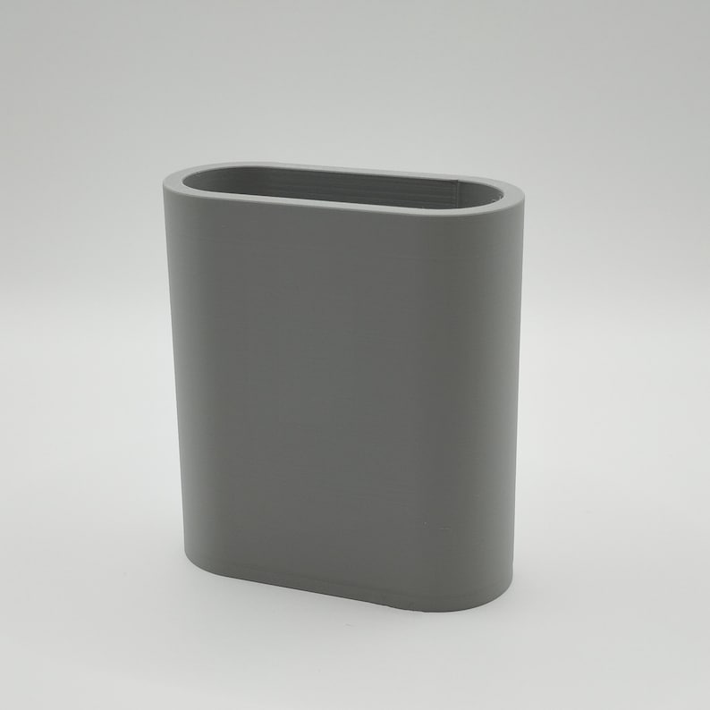 May include: A gray, oval-shaped container with a smooth surface. The container has rounded edges and a rectangular opening at the top. The object is a solid, neutral color and appears to be made of a durable material.