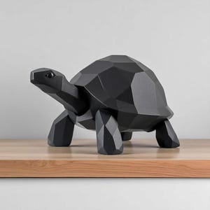 May include: A black geometric turtle sculpture with a faceted design. The decorative turtle is made of a solid material and stands on four legs. The sculpture is displayed on a wooden surface.