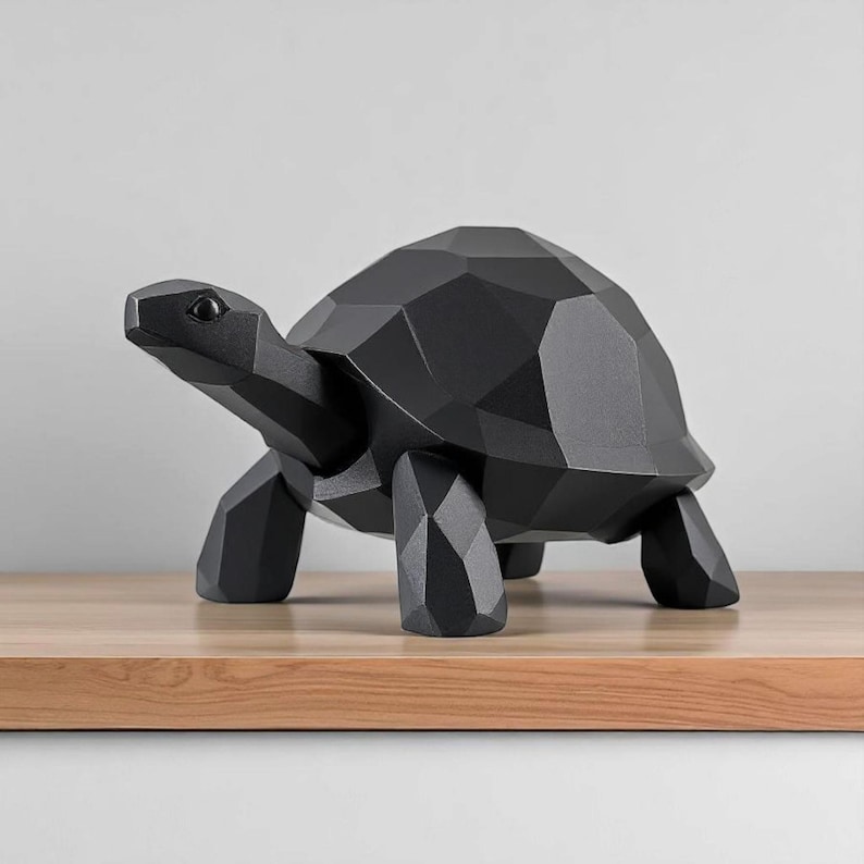 May include: A black geometric turtle sculpture with a faceted design. The decorative turtle is made of a solid material and stands on four legs. The sculpture is displayed on a wooden surface.