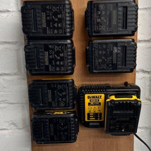 May include: A wooden rack holding several black and yellow DeWalt power tool batteries and a charger. The batteries are rectangular with the DeWalt logo and model information visible. The charger is yellow and black, with a digital display.