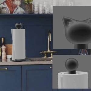 May include: A black cat-shaped paper towel holder. The holder features a black cat head on top and a black base. The paper towel roll is white. The holder is on a kitchen counter with blue cabinets and a gold faucet in the background.