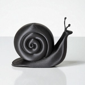 May include: A black snail figurine with a spiraled shell and two antennae. The snail is depicted in a smooth, matte finish, and is set against a white background. The figurine is a decorative item.