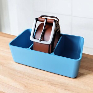 May include: A light blue plastic organizer with two compartments, one containing a brown leather belt with a silver buckle.