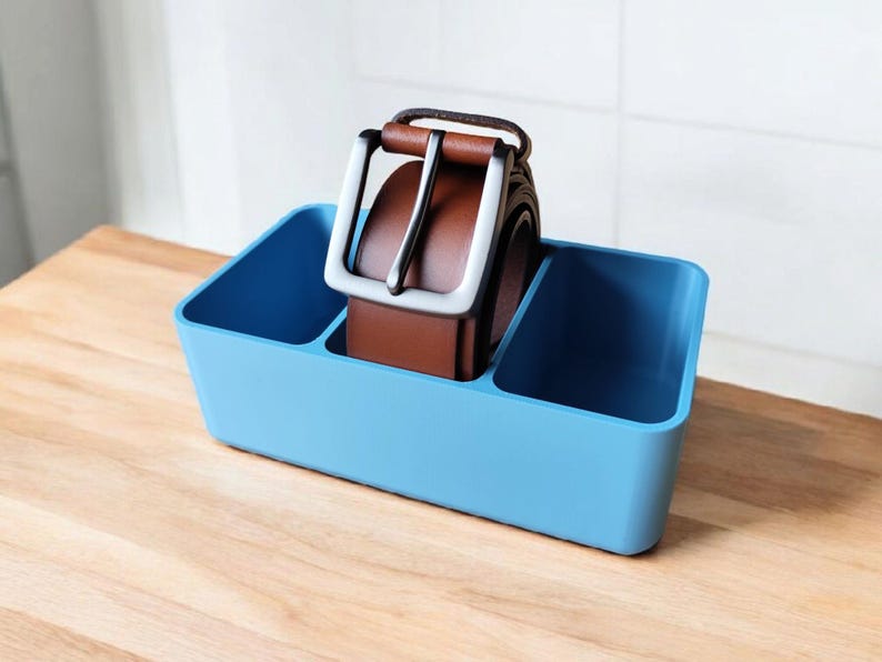 May include: A light blue plastic organizer with two compartments, one containing a brown leather belt with a silver buckle.