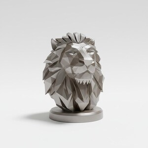 May include: A silver-colored, geometric lion head sculpture. The lion's mane and face are composed of angular planes, giving it a modern, faceted appearance. The sculpture sits on a circular base, creating a striking decorative piece.