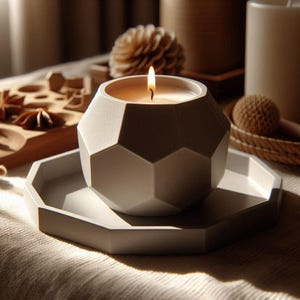 May include: A lit candle in a geometric, light gray container sits on a matching tray. The candle's flame glows brightly. Other decorative items, including a wooden star anise and a woven ball, are in the background. The overall theme is home decor.