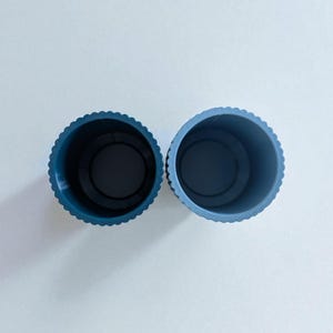 May include: Two blue plastic containers with a scalloped edge. The containers are cylindrical with a dark interior. The containers are side by side against a white background.