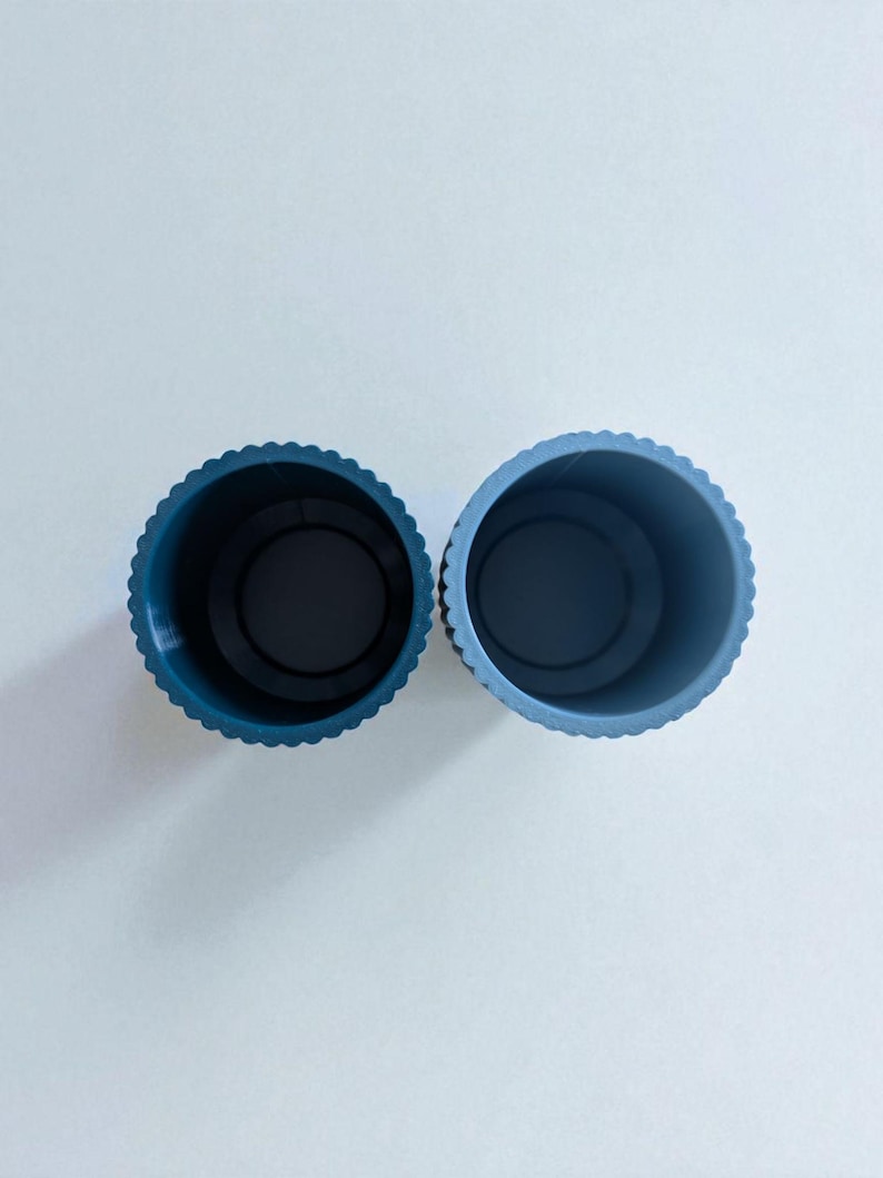 May include: Two blue plastic containers with a scalloped edge. The containers are cylindrical with a dark interior. The containers are side by side against a white background.