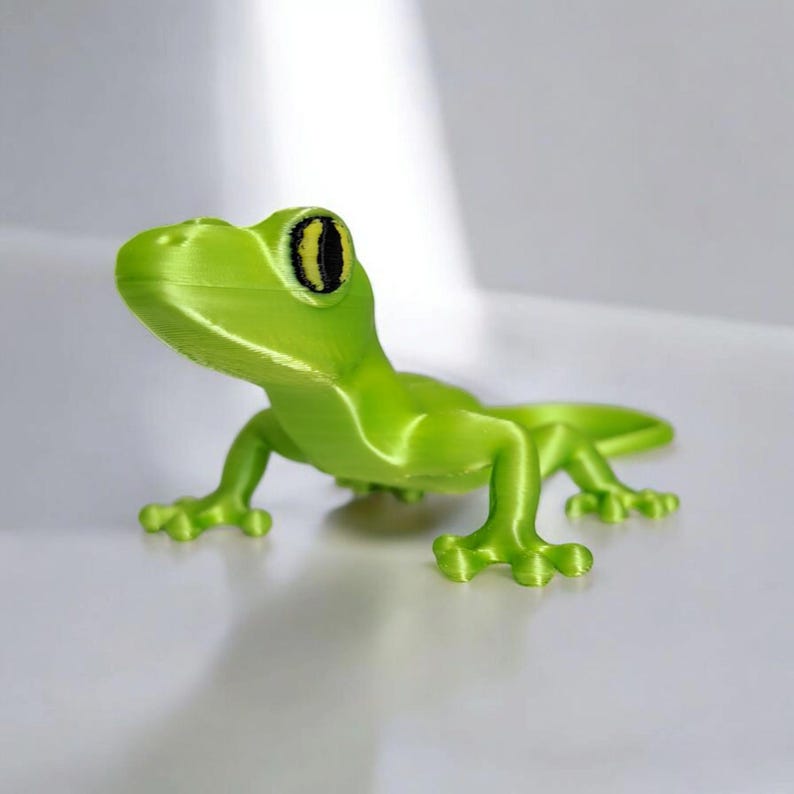 May include: A bright green gecko figurine with a detailed, textured surface. The gecko has a curved body, four legs, and a long tail. Its eyes are black with yellow accents. The figurine is a decorative item.