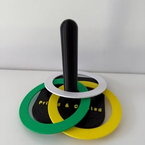 May include: A black and white ring toss game with green and yellow rings. The rings are stacked on a black pole. The text "Prid & O ted" is visible on the black base.