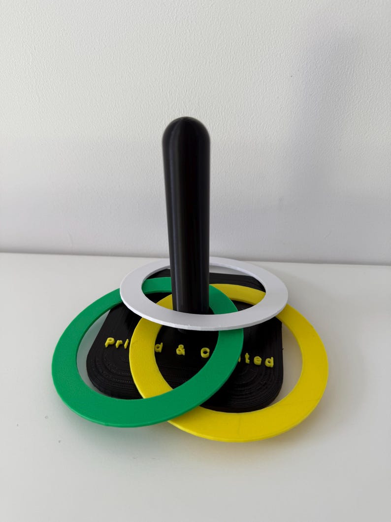 May include: A black and white ring toss game with green and yellow rings. The rings are stacked on a black pole. The text "Prid & O ted" is visible on the black base.