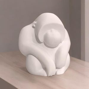 以下が含まれることがあります： 白い抽象彫刻。座った人物で、頭は膝の上に置かれています。彫刻は滑らかで丸みを帯びた形で、明るい色の木製の表面に置かれています。