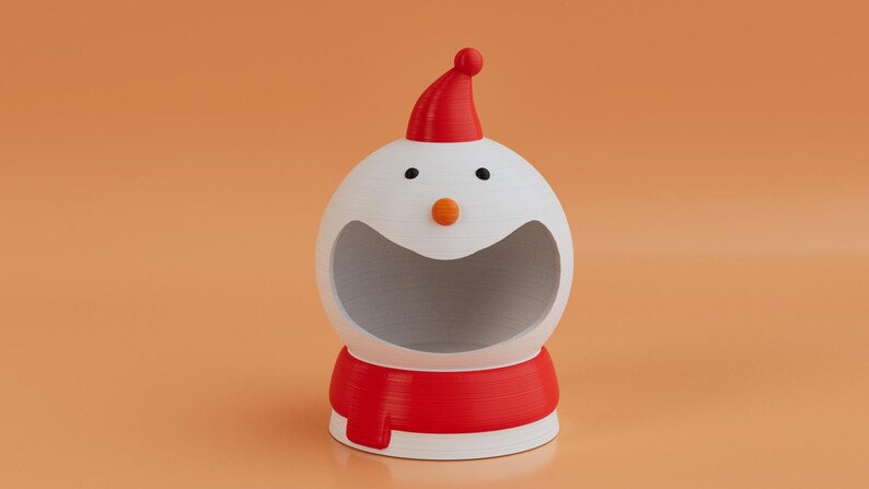 May include: A novelty snowman-shaped container, featuring a red hat and scarf. The white body has black eyes and an orange nose. The container has a large opening, ideal for storage or display. A festive item for seasonal decor.