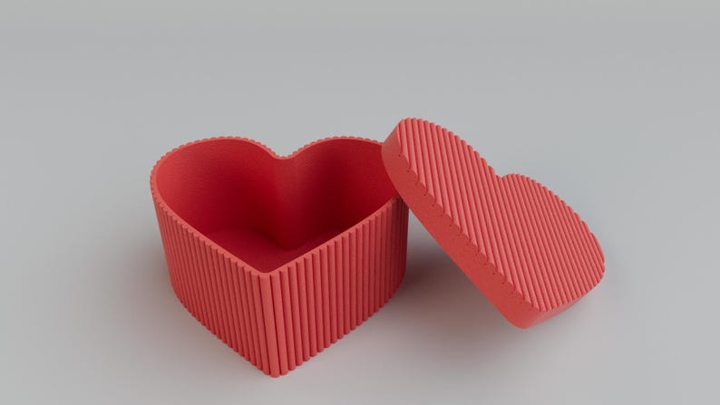 Pu&ograve; includere: Scatola a forma di cuore rosso corallo con coperchio abbinato, leggermente aperta. La scatola e il coperchio hanno una texture a coste. Lo sfondo &egrave; grigio chiaro. Ideale per regali o gioielli.