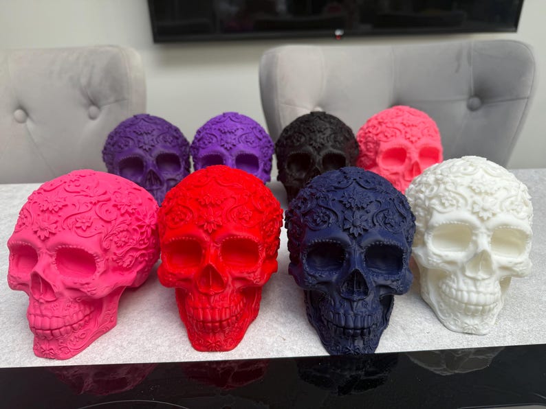 May include: A collection of decorative skull figurines in various colors, including pink, red, purple, black, blue, and white. Each skull features intricate floral patterns and detailed facial features, suitable for home decor.