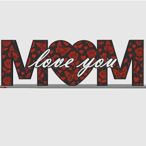 May include: A decorative sign spelling "MOM" with the words "love you" in cursive. The letters are black with a red floral and butterfly pattern. The heart-shaped "O" is also patterned. A thoughtful gift.