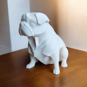 K&ouml;nnte beinhalten: Eine wei&szlig;e Mops-Hundeskulptur mit einem stilisierten, geometrischen Design. Der Hund sitzt auf einer Holzoberfl&auml;che. Die Skulptur hat eine glatte Oberfl&auml;che und ist ein dekorativer Gegenstand.