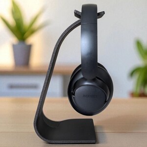 Peut inclure: Un support de casque noir au design incurv&eacute;, tenant une paire de casques noirs. Les &eacute;couteurs portent la marque "BERIBES". Le support est pos&eacute; sur une surface en bois, avec un arri&egrave;re-plan flou.