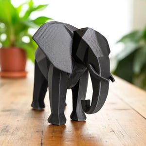 Op de afbeelding: Een zwarte geometrische olifantenfiguur. De sculptuur heeft een facetontwerp, met scherpe hoeken en vlakken die de vorm van de olifant cre&euml;ren. De olifant staat op een houten oppervlak.