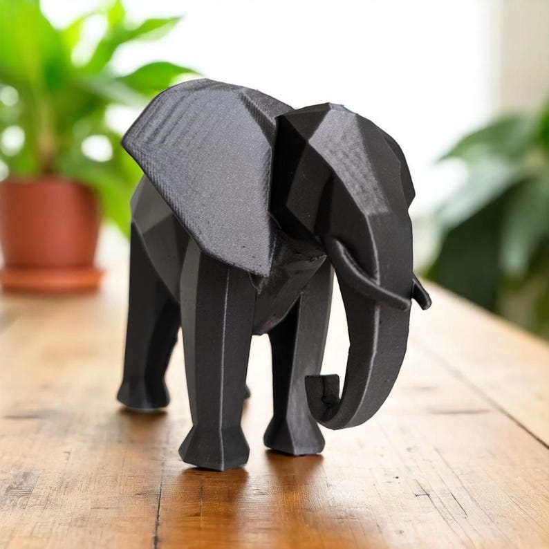 Op de afbeelding: Een zwarte geometrische olifantenfiguur. De sculptuur heeft een facetontwerp, met scherpe hoeken en vlakken die de vorm van de olifant cre&euml;ren. De olifant staat op een houten oppervlak.