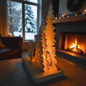 May include: A white, laser-cut Christmas tree and reindeer candle holder on a wooden table. The candle holder has a warm glow from the lit candle inside. A cozy fireplace and snowy window are in the background, creating a festive holiday scene.