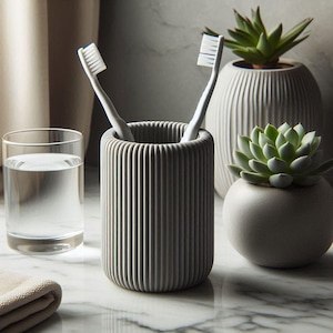 May include: A gray, ribbed toothbrush holder with two white toothbrushes. A glass of water and two small potted succulents are also visible. The items are arranged on a marble surface, creating a clean, modern aesthetic.