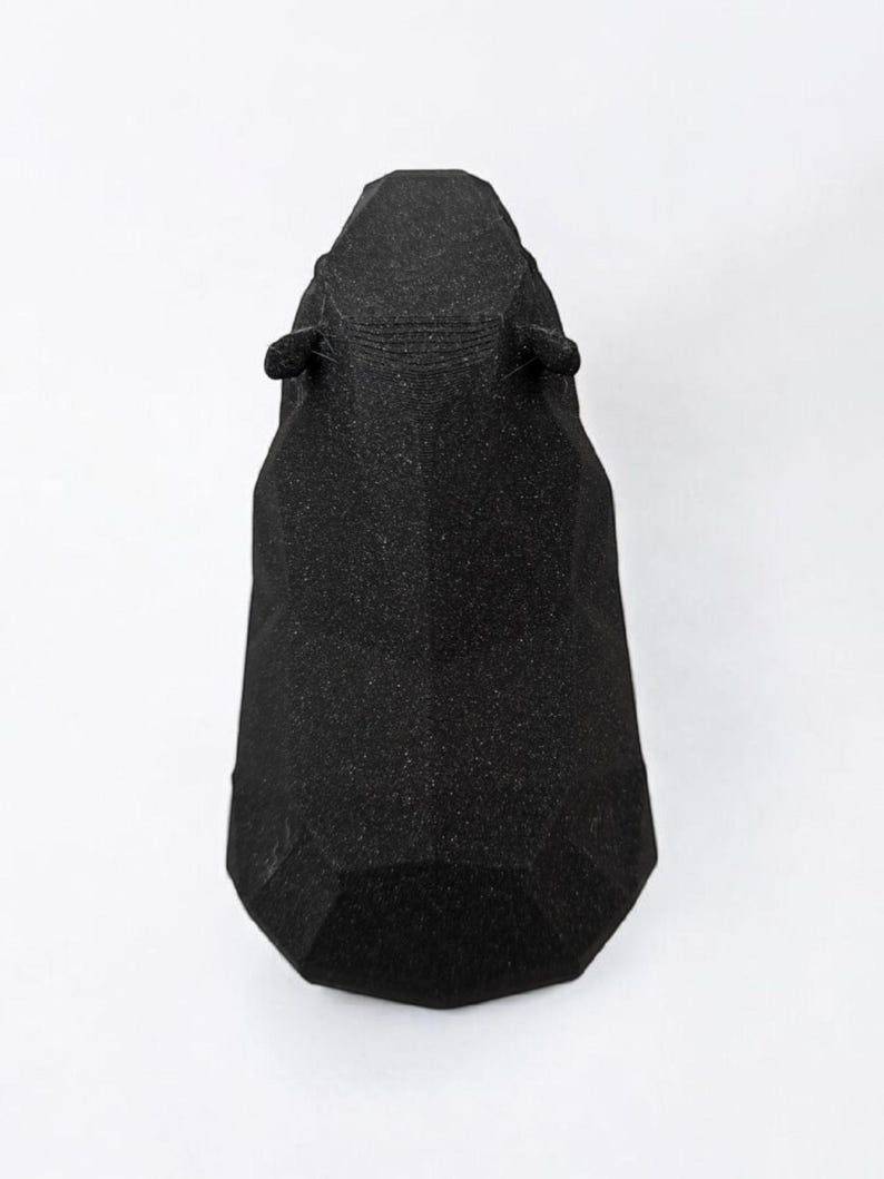 May include: A black, geometric sculpture of an animal head, possibly a horse or a similar mammal. The sculpture has a textured surface and is set against a white background. The ears are small and rounded.