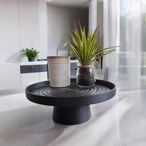 May include: A black, round, tiered serving tray holds a candle and a small potted plant. The candle has a wooden lid and the text "Mindfull" and "n&deg;21". A small glass jar with a plant is also on the tray.