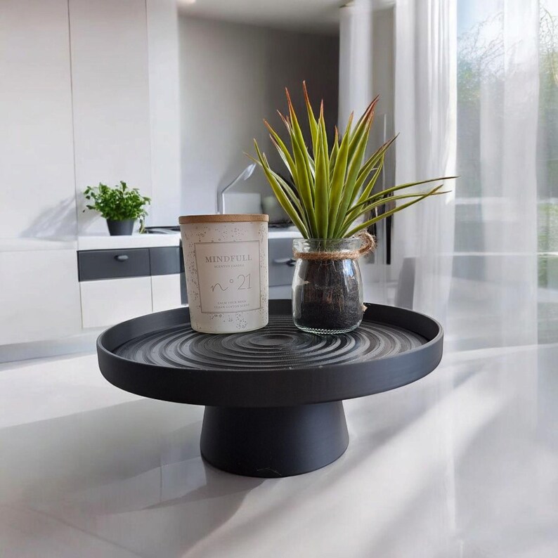 May include: A black, round, tiered serving tray holds a candle and a small potted plant. The candle has a wooden lid and the text "Mindfull" and "n&deg;21". A small glass jar with a plant is also on the tray.