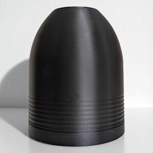 May include: A matte black, bullet-shaped object with a rounded top and a series of horizontal, grooved bands near the base. The object is set against a plain white background, with a shadow to the left.
