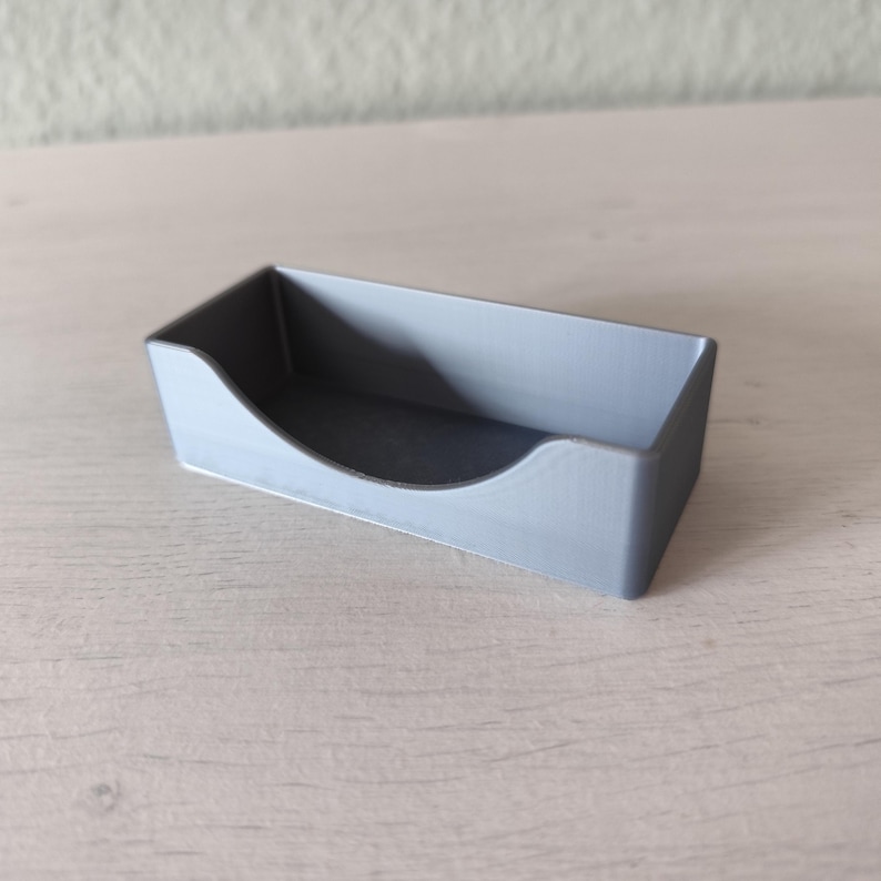 Pu&ograve; includere: Un piccolo vassoio rettangolare grigio chiaro con un ritaglio curvo su un lato. Il vassoio &egrave; realizzato in un materiale solido e ha una superficie liscia. Il vassoio &egrave; progettato per contenere piccoli oggetti.