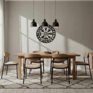 Peut inclure: Une salle &agrave; manger avec une table et des chaises en bois clair, pos&eacute;es sur un tapis &agrave; motifs. Trois lampes suspendues noires sont suspendues au-dessus de la table. Une pi&egrave;ce murale d&eacute;corative et une table d'appoint compl&egrave;tent la pi&egrave;ce.