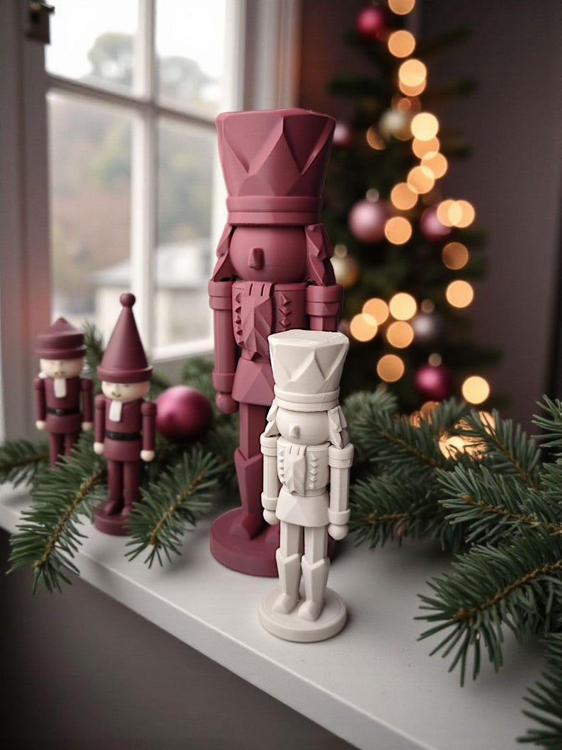 May include: A collection of decorative nutcrackers in various sizes and colors, arranged on a windowsill. The nutcrackers are primarily burgundy and white, with intricate details. A Christmas tree with ornaments and lights is visible in the background, along with evergreen branches.