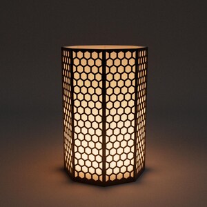 Op de afbeelding: Een cilindervormige lamp met een honingraatpatroon. De lamp is gemaakt van donkerbruin materiaal en straalt een warm, zacht licht uit. Het geometrische ontwerp cre&euml;ert een visueel aantrekkelijk effect, geschikt voor interieurdecoratie.