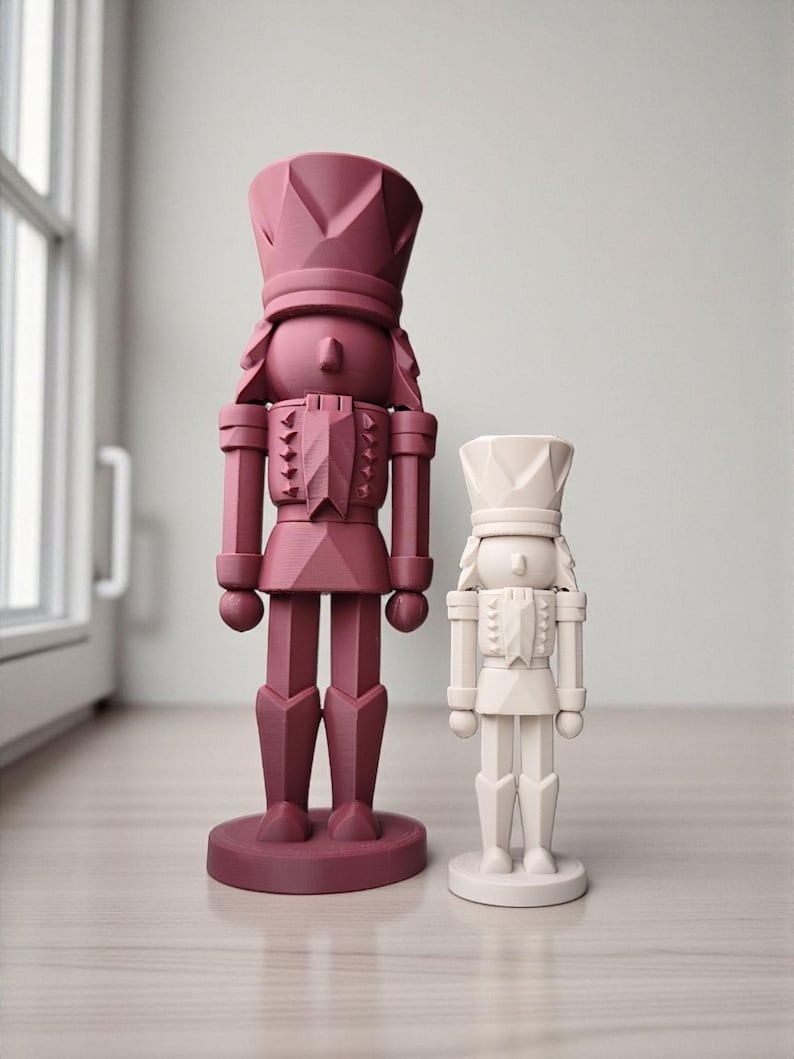May include: Two decorative nutcrackers in a modern style. One is a deep burgundy color, and the other is off-white. Both have a geometric design and stand on a round base. The larger nutcracker is approximately 12 inches tall.