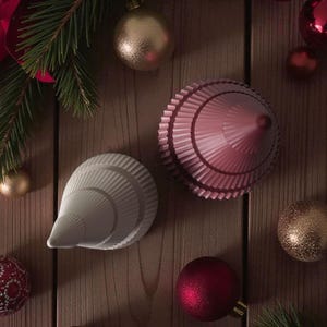 May include: A festive arrangement featuring Christmas ornaments and decorative objects. The image showcases red and gold baubles, along with two unique, cone-shaped ornaments in white and pink. Green pine branches add a seasonal touch to the wooden background.